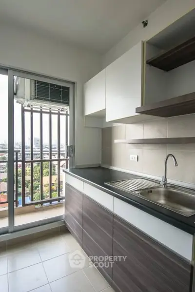 Modern kitchen with sleek cabinetry and balcony view in urban apartment.