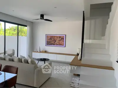 Modern living room with sleek staircase and stylish decor, featuring large windows and contemporary furniture.