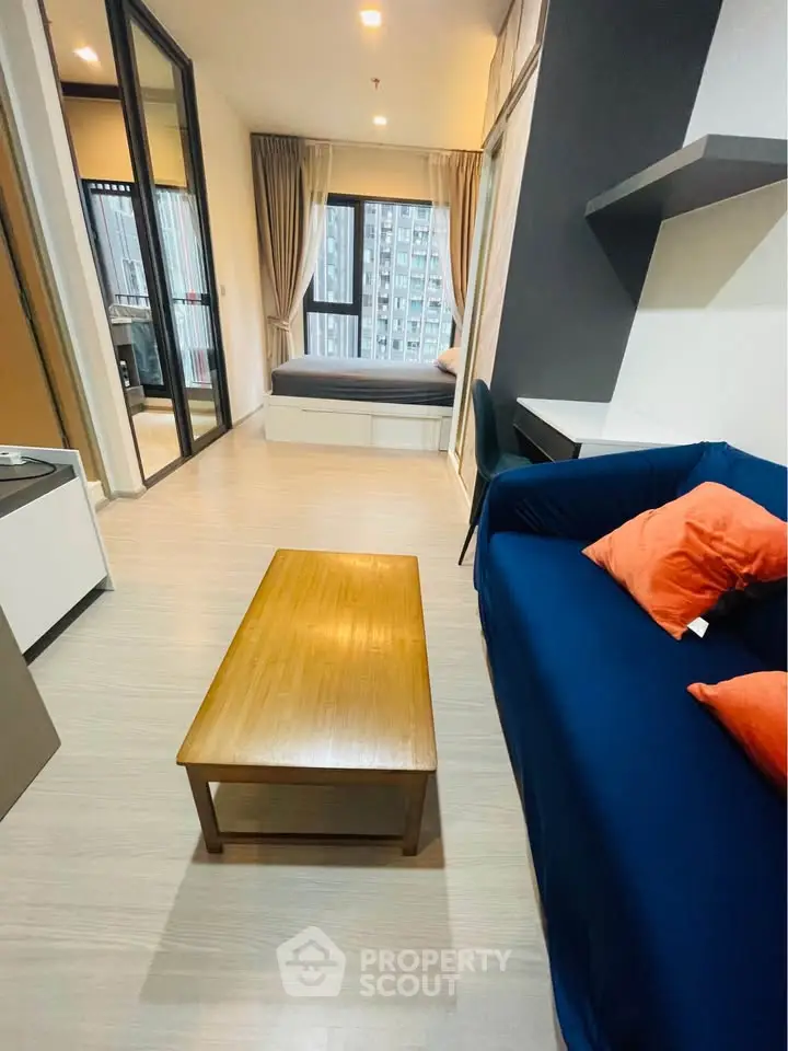 Modern living room with blue sofa, wooden coffee table, and large window view in a stylish apartment.