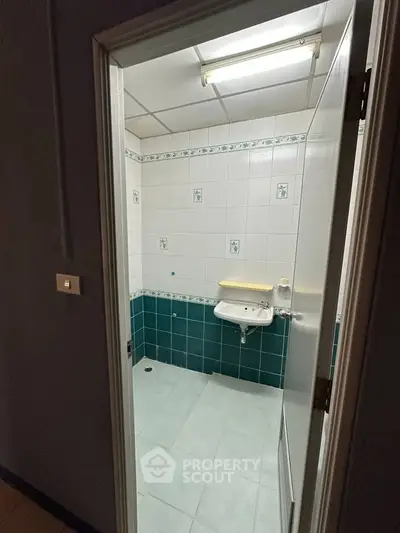 Compact bathroom with teal and white tiles and wall-mounted sink.