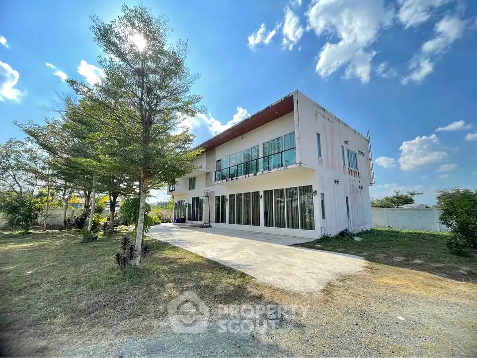 Modern two-story house with large windows and spacious outdoor area under a clear blue sky.