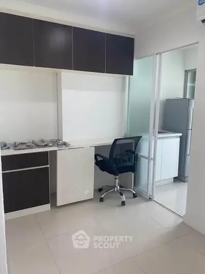 Modern kitchen with sleek cabinetry and office chair, featuring a gas stove and refrigerator.