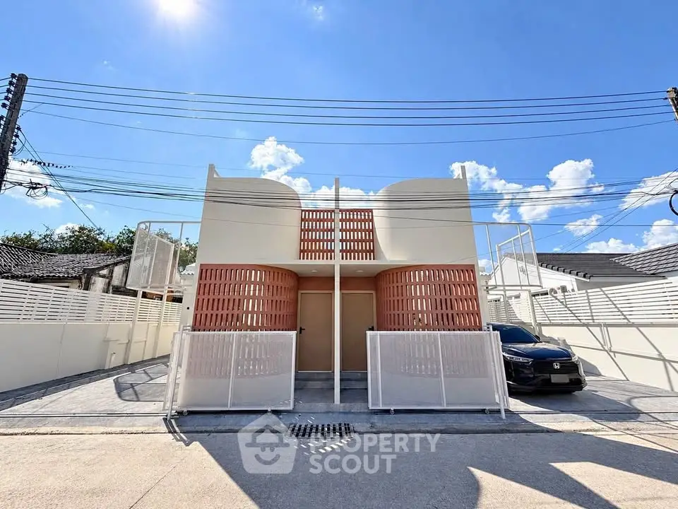 Modern architectural home exterior with unique design and gated driveway under a clear blue sky.