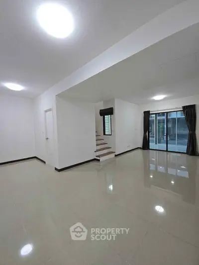 Spacious modern living room with large windows and staircase, perfect for family gatherings.