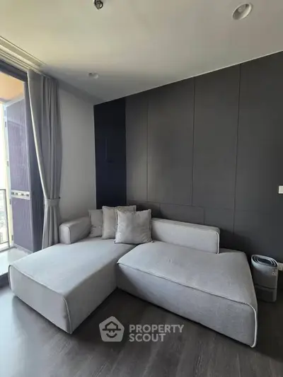 Modern living room with sleek gray sectional sofa and floor-to-ceiling windows offering natural light.