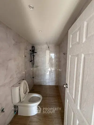 Modern bathroom with sleek marble tiles and wooden flooring, featuring a shower and toilet.