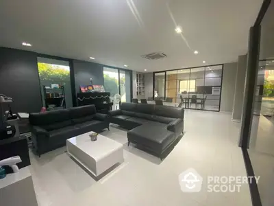 Spacious modern living room with sleek black leather sofas, gleaming white tiles, and an open layout leading to a well-equipped kitchen.