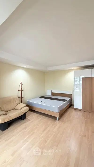 Spacious bedroom with wooden flooring, modern bed, and cozy sofa, perfect for relaxation.