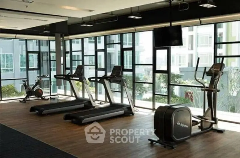 Spacious modern gym with large windows and exercise equipment in luxury apartment building.