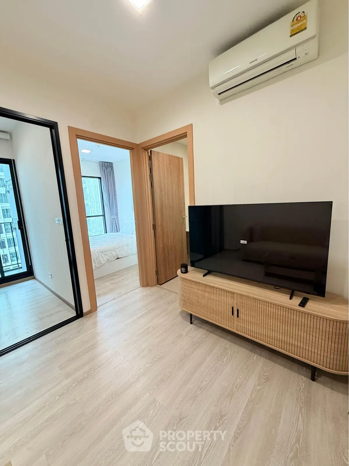 Modern living room with sleek TV and air conditioning, leading to a cozy bedroom with natural light.