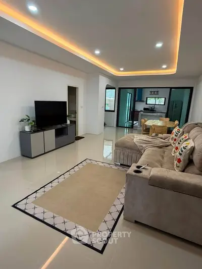 Spacious modern living room with cozy sofa and sleek TV setup, leading to an open kitchen area.