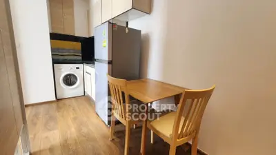Cozy kitchen with wooden flooring, dining table, fridge, and washing machine.