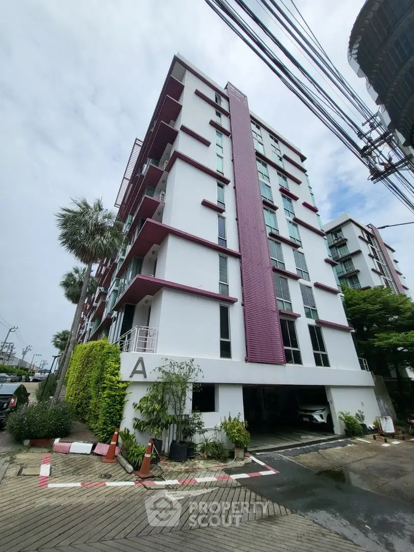 Modern multi-story residential building with lush greenery and parking area.