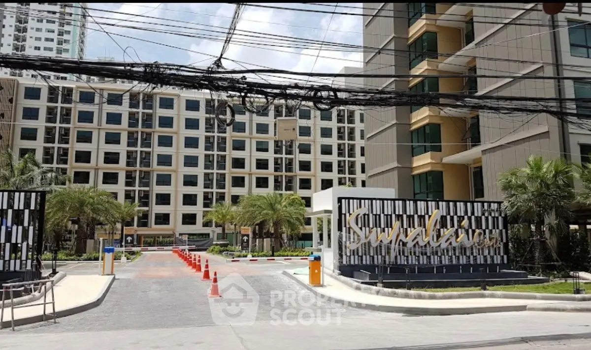 Modern condominium entrance with palm trees and stylish signage in urban setting.