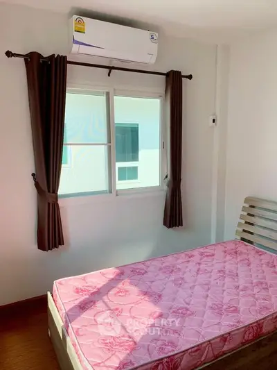 Cozy bedroom with air conditioning and natural light, featuring a simple bed setup and window view.