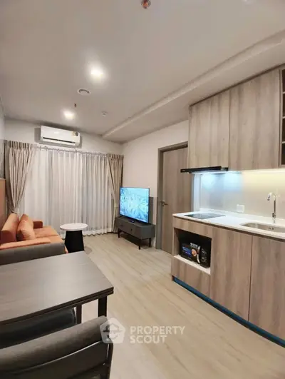 Modern living room with open kitchen, featuring sleek cabinetry and cozy seating area.