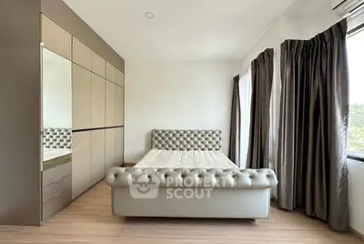 Spacious bedroom with elegant tufted bed and large wardrobe, featuring natural light and modern decor.