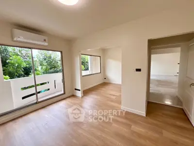 Spacious living room with wooden flooring and large windows offering lush garden views.