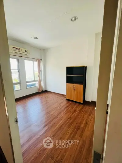 Spacious empty room with wooden flooring and large windows, perfect for customization.
