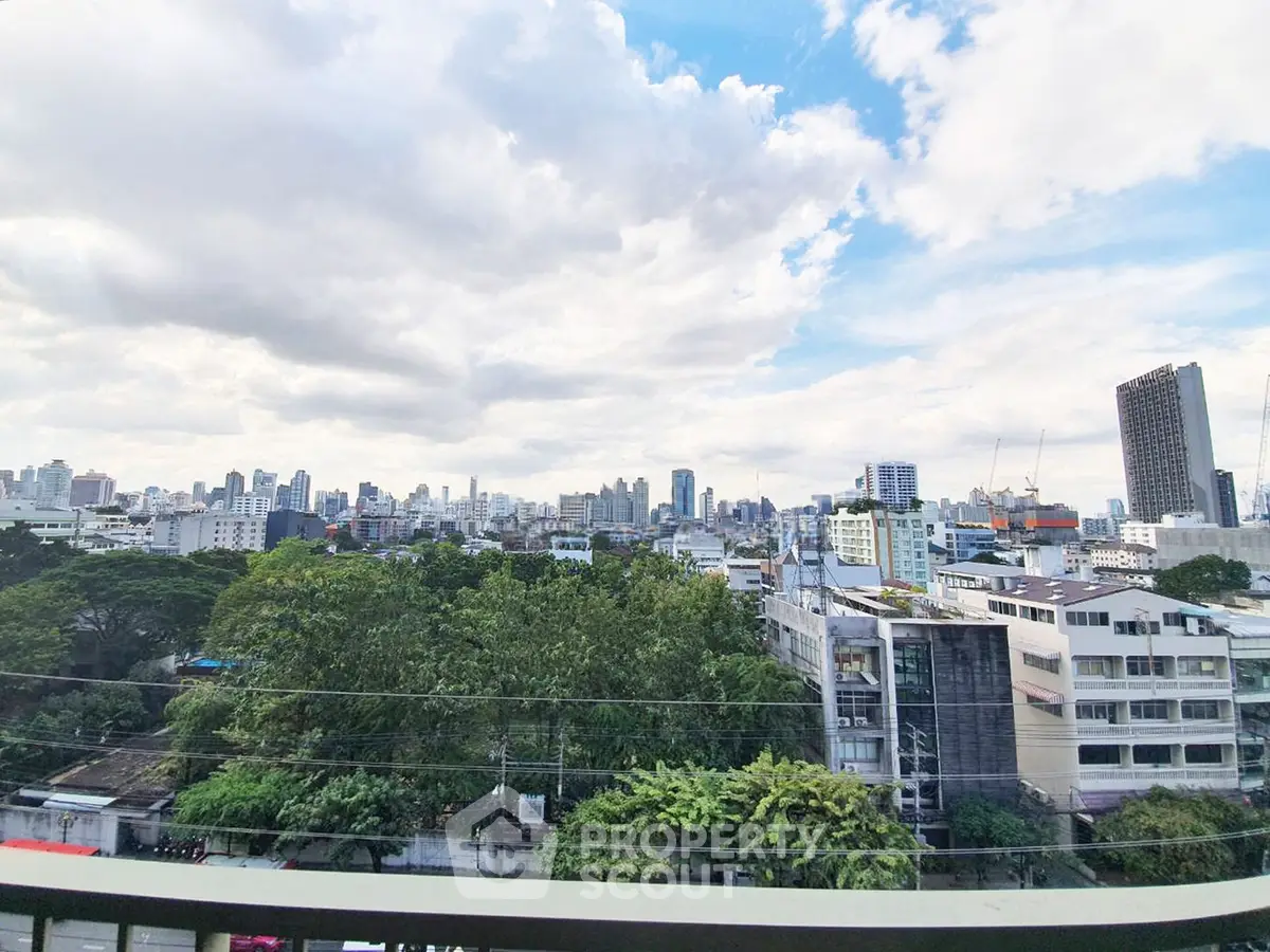 Stunning cityscape view from a high-rise balcony overlooking lush greenery and urban skyline.