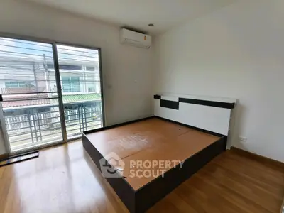 Spacious bedroom with large window and wooden flooring, featuring a modern bed frame.