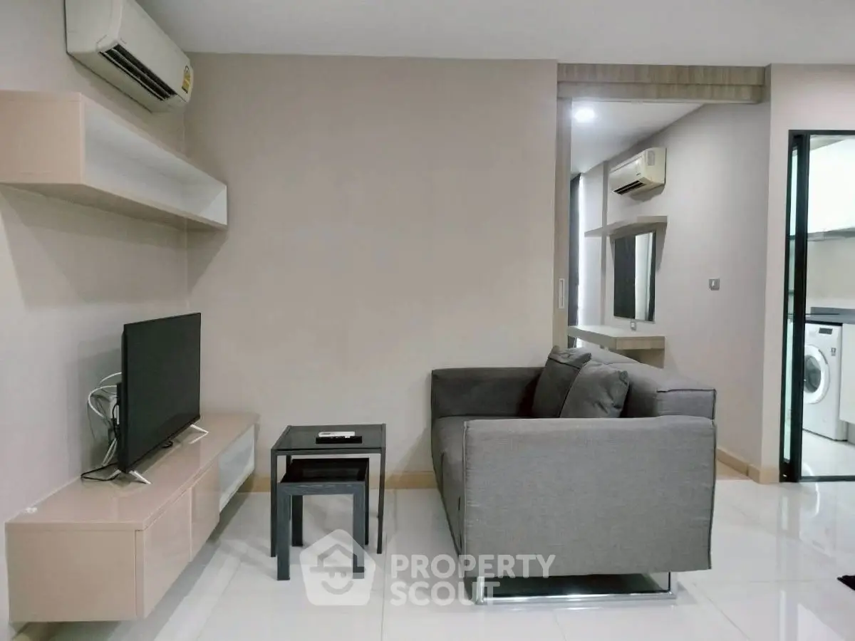 Modern living room with sleek furniture and air conditioning, adjacent to a kitchen with washing machine.