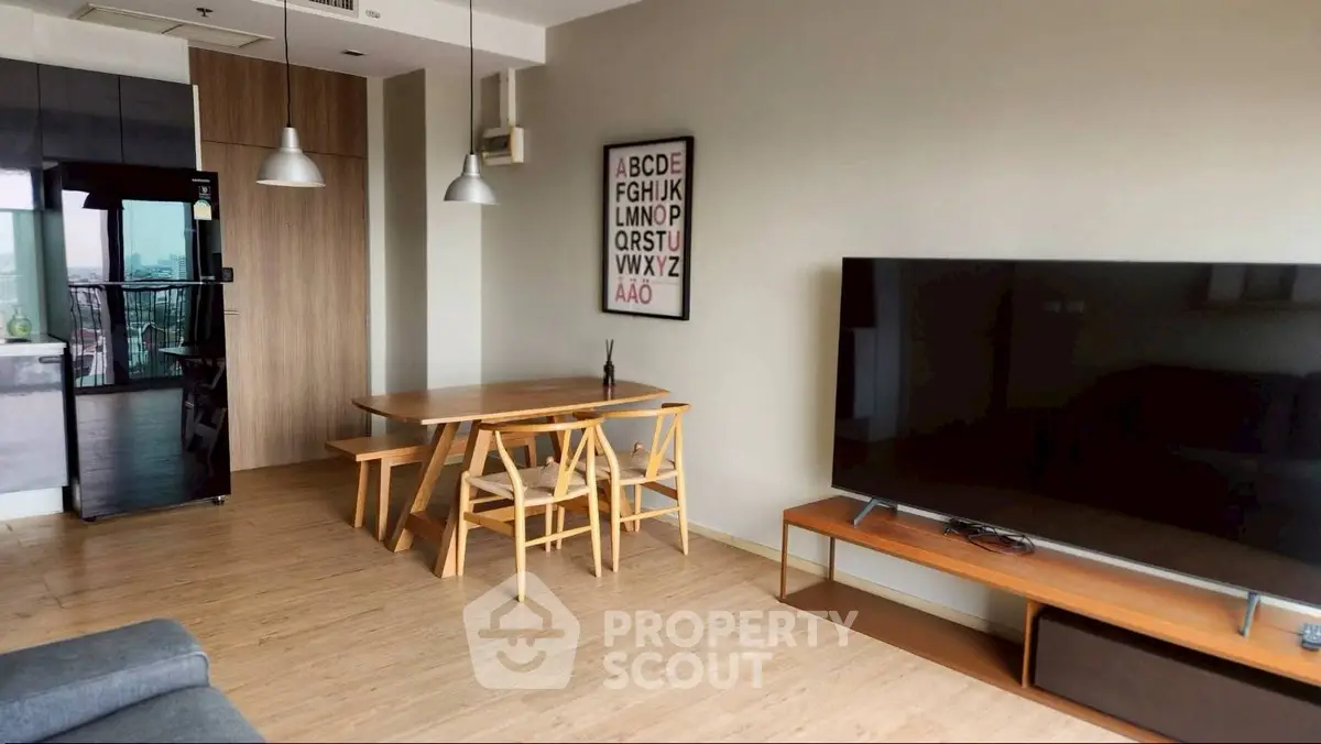 Modern living room with stylish furniture and large TV, featuring a cozy dining area and sleek wooden flooring.