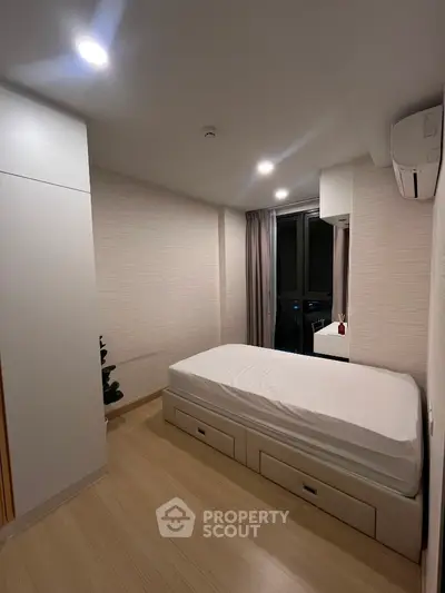 Modern minimalist bedroom with single bed and built-in storage, featuring sleek design and natural light.