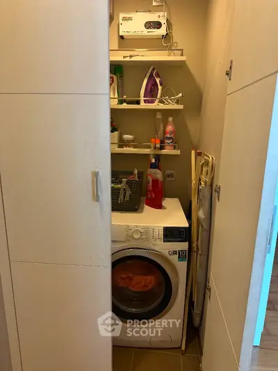 Compact laundry area with washing machine and storage shelves in modern apartment.