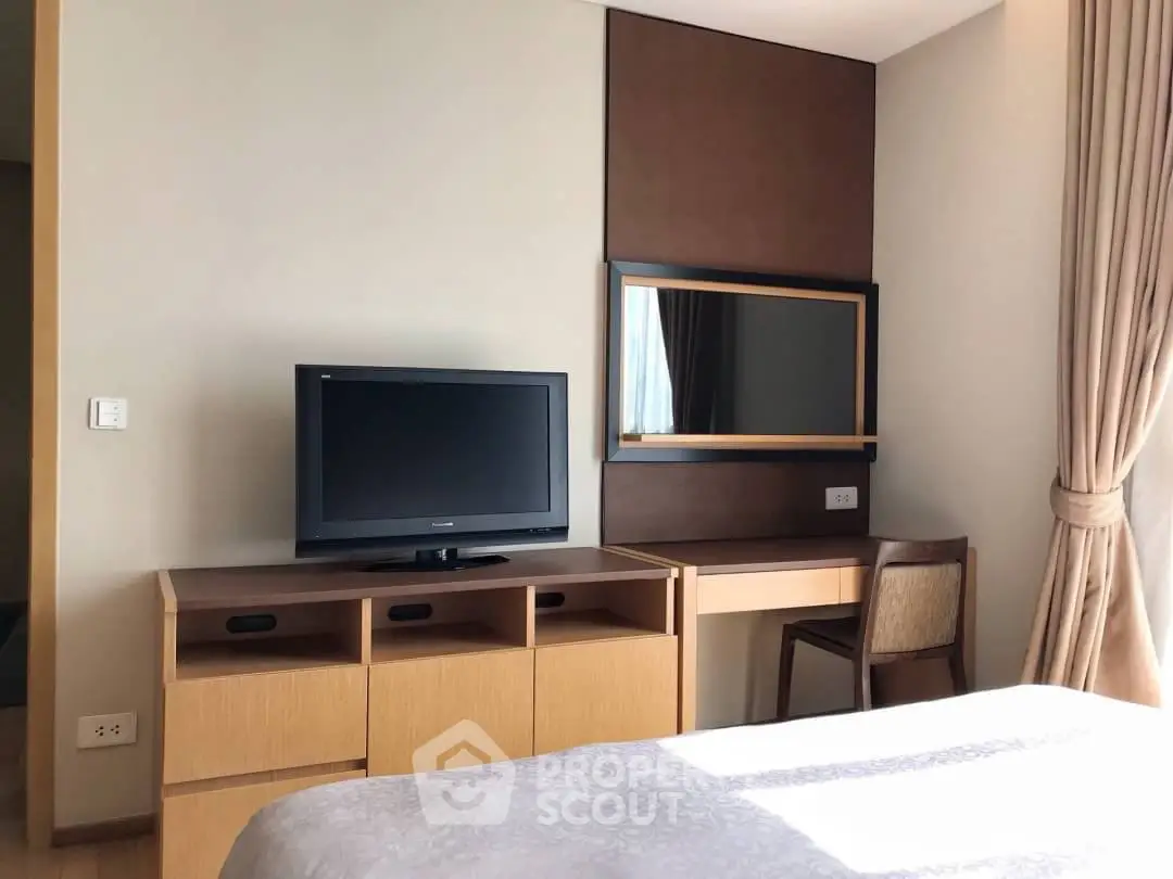 Modern bedroom with TV and desk, featuring natural light and elegant curtains.