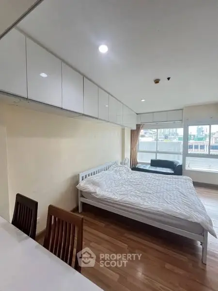 Modern studio apartment with cozy bed and city view, featuring sleek wooden flooring and ample natural light.