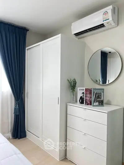 Modern bedroom with sleek white furniture and air conditioning, featuring a stylish mirror and elegant decor.