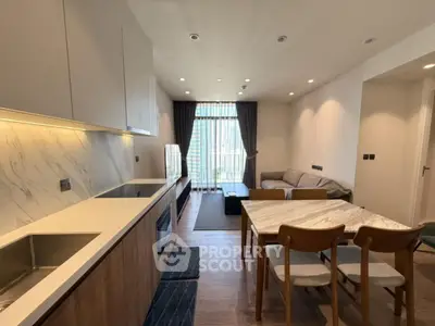 Modern open-layout living room with stylish kitchen and dining area, featuring elegant furnishings and natural light.