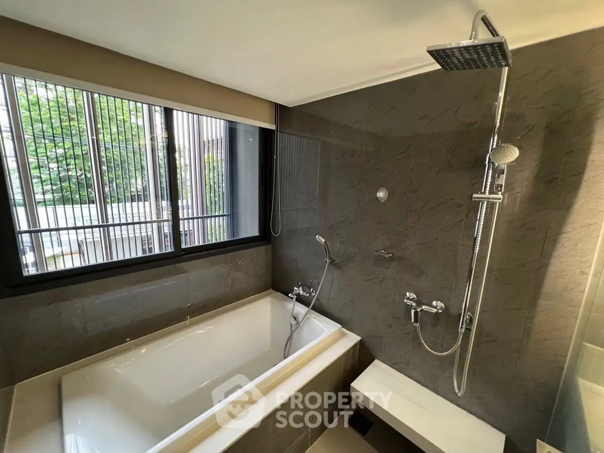 Luxurious bathroom with modern bathtub and rain shower, featuring elegant tile design and large window view.