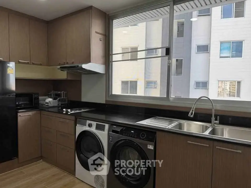 Modern kitchen with sleek cabinetry, washer, dryer, and large window view.