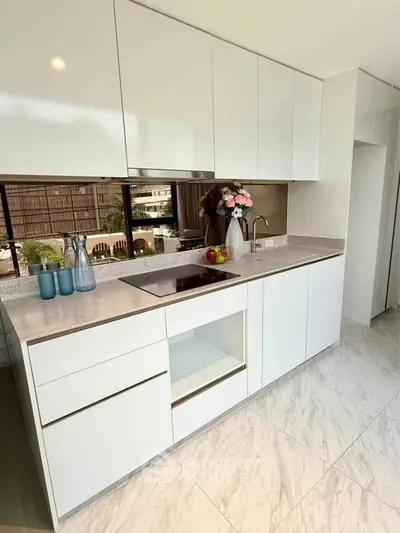 Modern kitchen with sleek white cabinets and marble flooring, featuring a built-in electric stove and stylish decor.