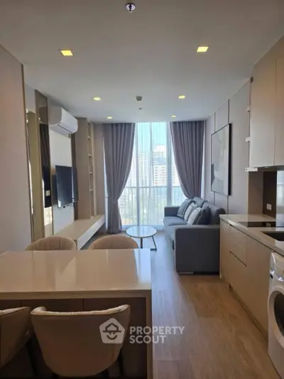 Modern living room with open kitchen, stylish furniture, and city view from large window.