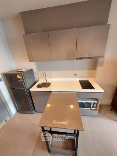 Modern kitchen with sleek cabinets, compact fridge, and electric cooktop in a stylish apartment.