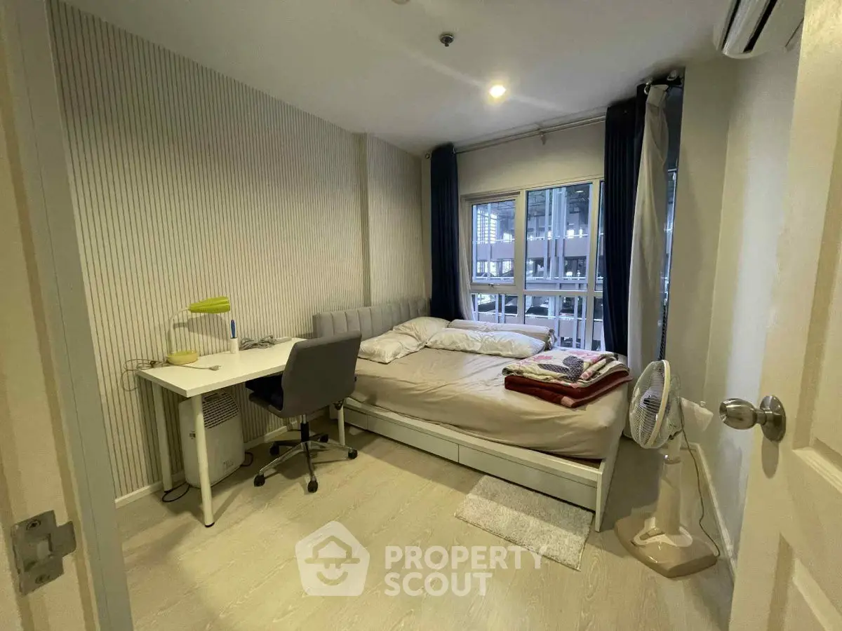 Modern bedroom with study desk and large window view in urban apartment.