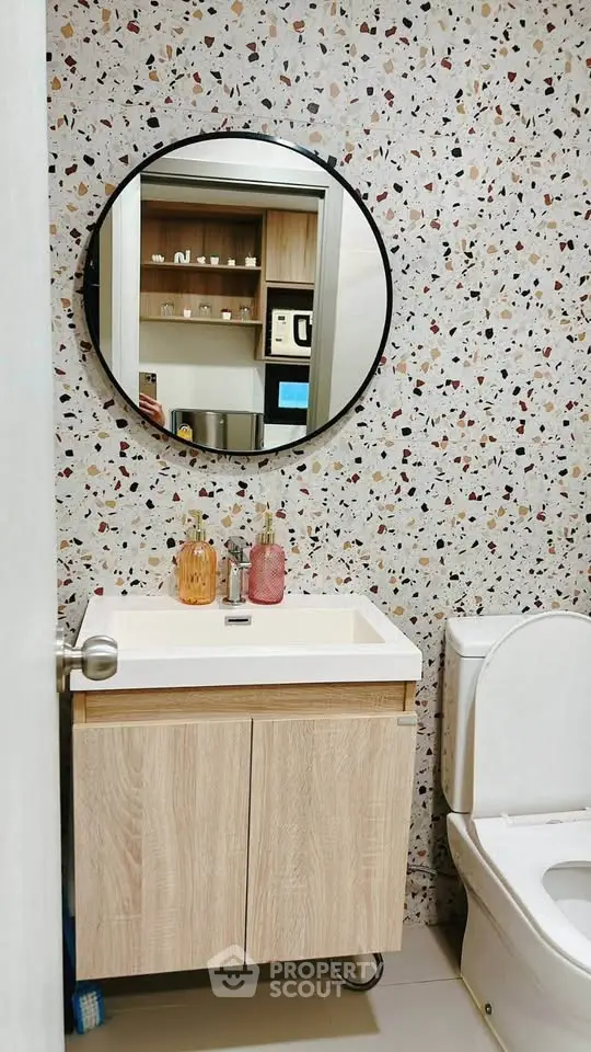Stylish bathroom with terrazzo wall, round mirror, and modern fixtures.
