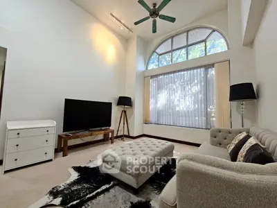 Spacious living room with high ceiling and large window, featuring modern furniture and stylish decor.