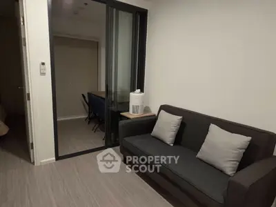 Modern living room with sleek gray sofa and sliding glass doors leading to a study area.