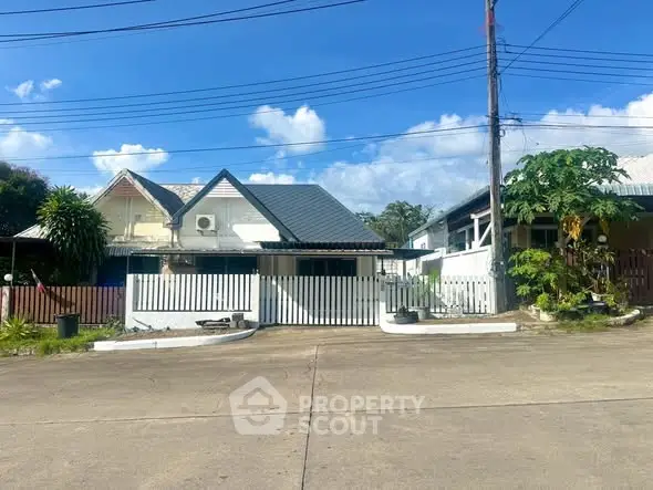 Charming suburban house with a fenced yard and lush greenery under a clear blue sky.
