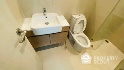 Compact modern bathroom with sleek fixtures, including a wall-mounted sink and a white toilet, complemented by beige wall tiles for a clean look.