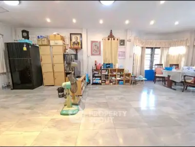 Spacious living room with tiled flooring and ample natural light, featuring storage cabinets and a fan.