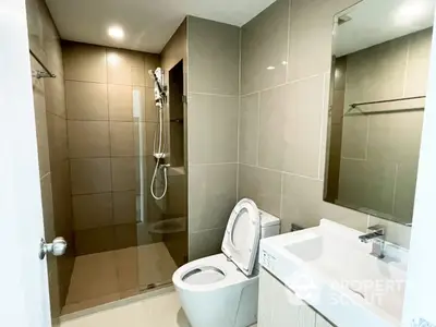 Modern bathroom with wall-mounted shower, sleek toilet, and a stylish sink with a large mirror, featuring neutral tilework for a serene ambiance.