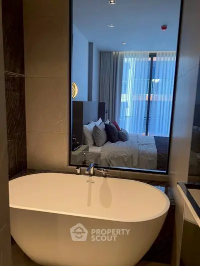 Luxurious bathroom with freestanding bathtub and view into modern bedroom.