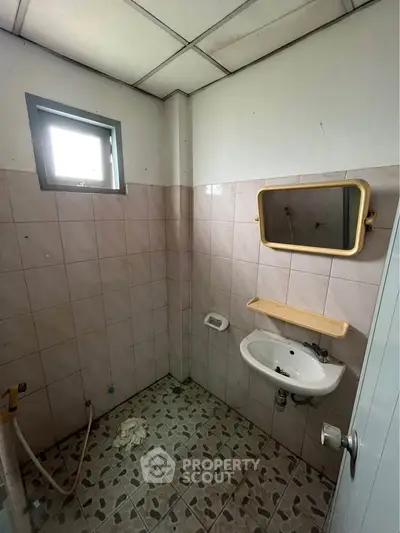 Compact bathroom with tiled walls and floor, featuring a small sink and mirror.