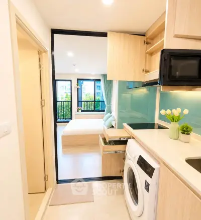 Modern studio apartment with open kitchen and washing machine, featuring a cozy bedroom and balcony view.