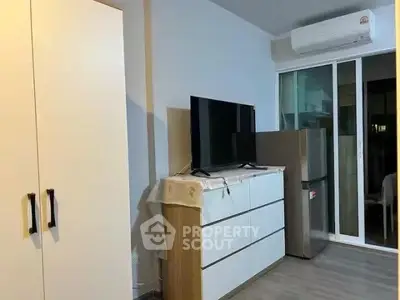 Modern apartment interior with TV, dresser, and sliding glass door to balcony.